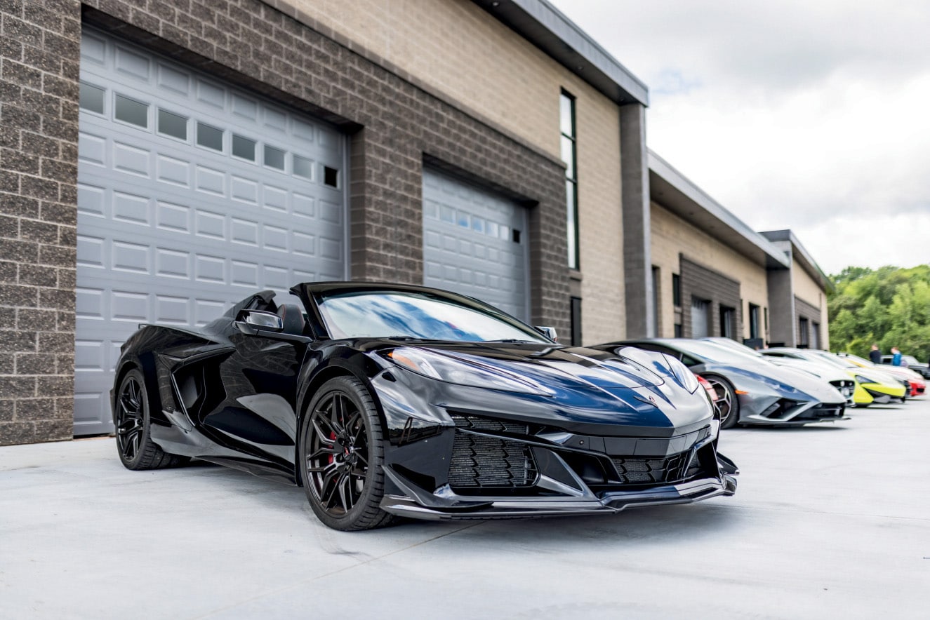 A Corvette and a row of sports cars lined up outside the overhead doors at The Hide Out