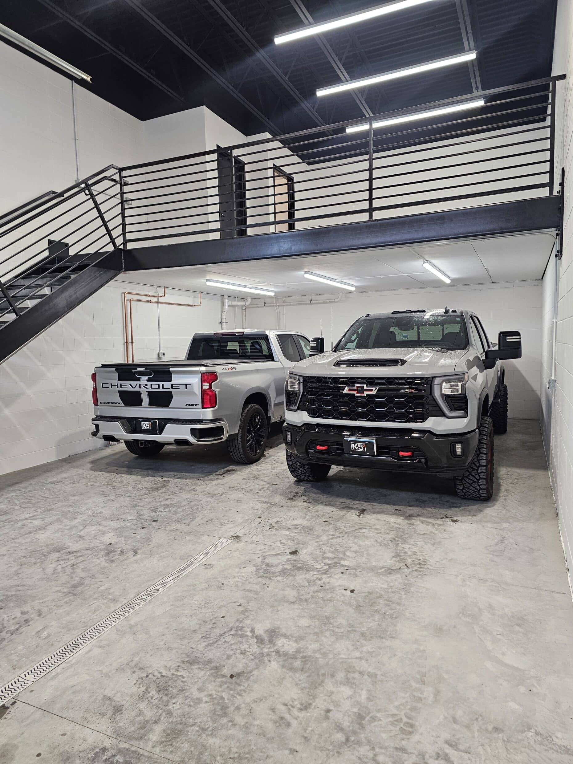 Two full-size pickup trucks parked side by side inside a Hide Out garage suite