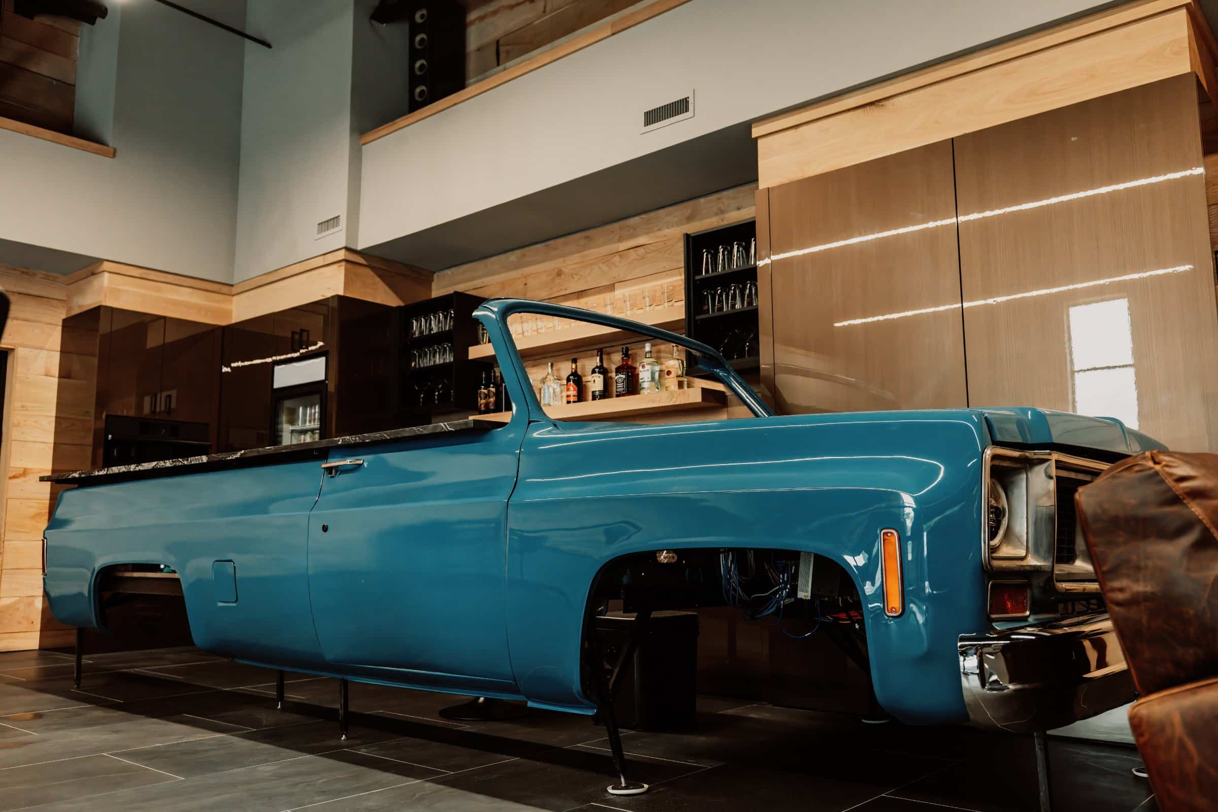 Blue squarebody truck parked beside a finished bar inside a Hide Out garage suite