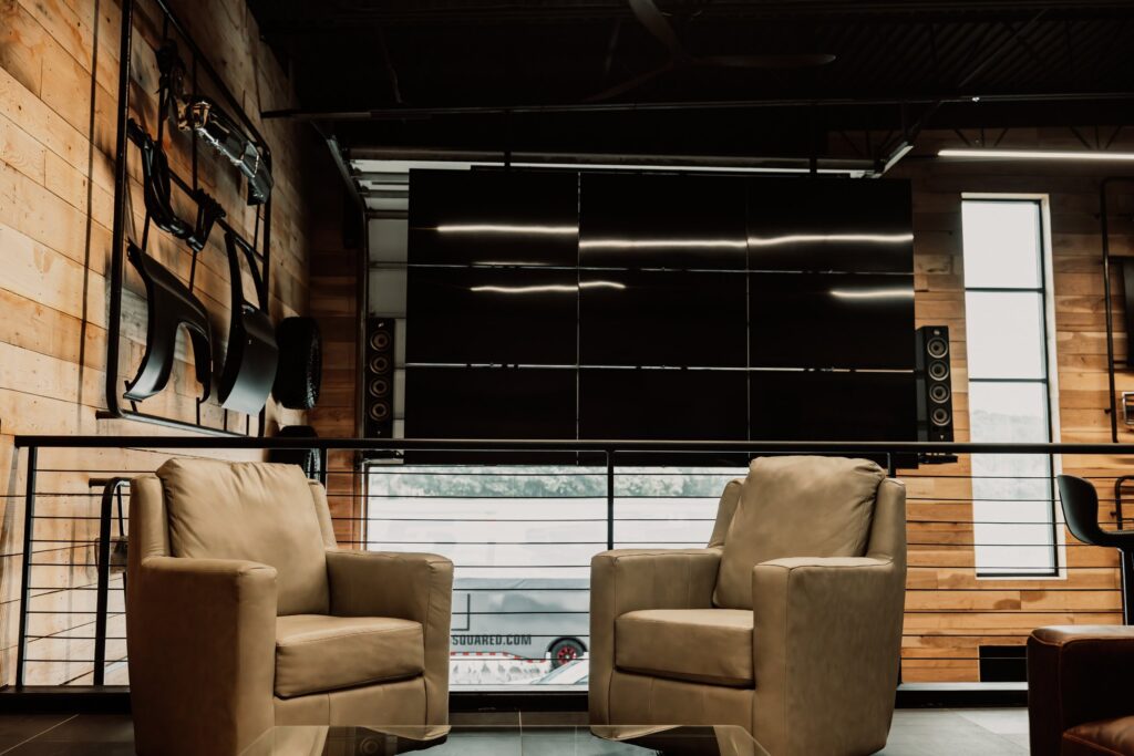 Finished garage condo lounge with a large screen wall and seating at The Hide Out